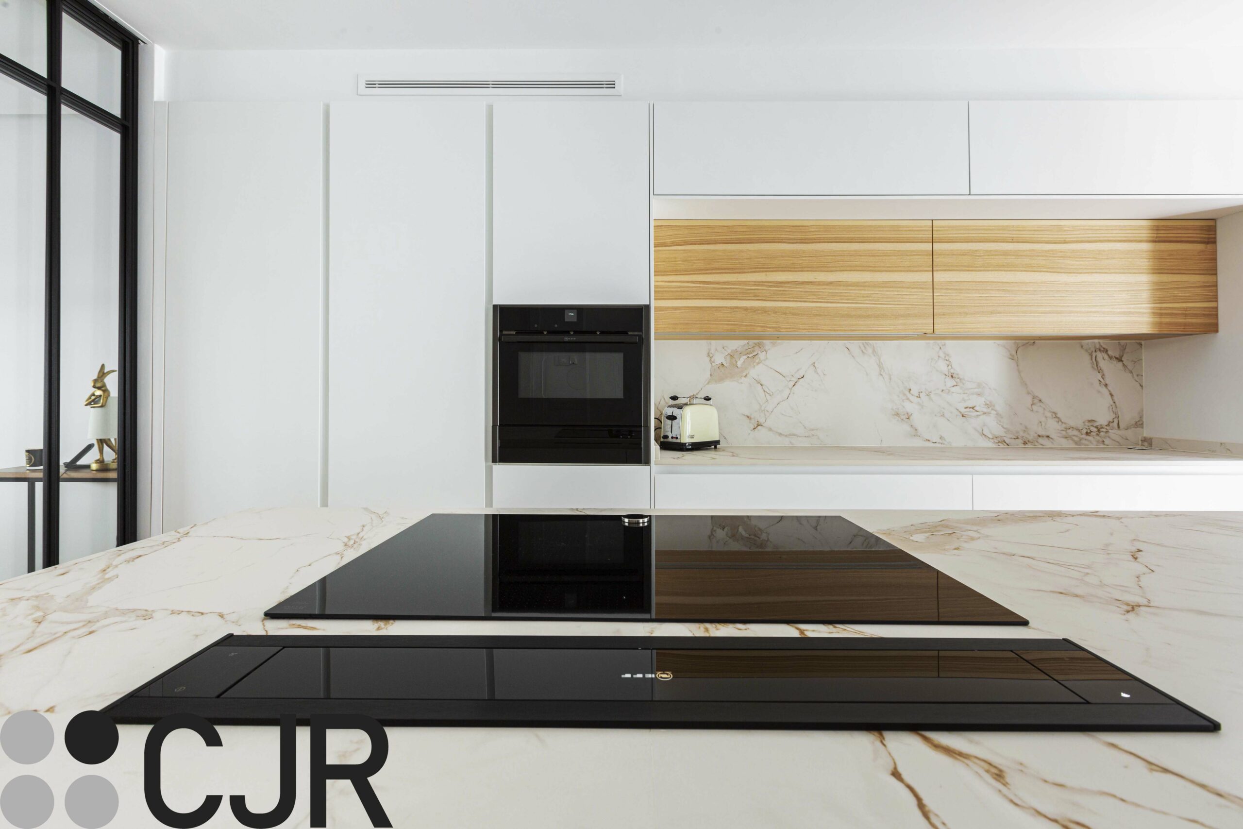 cocina moderna blanca y madera con placa y campana escamoteable de neff sobre encimera dekton entzo cocinas cjr